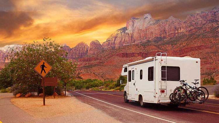 RV on the road with mountains and sunset.
