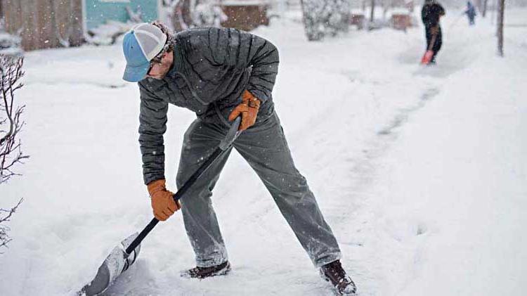 Business owner shoveling snow to clear a sidewalk in order to prevent slip and falls in the workplace.