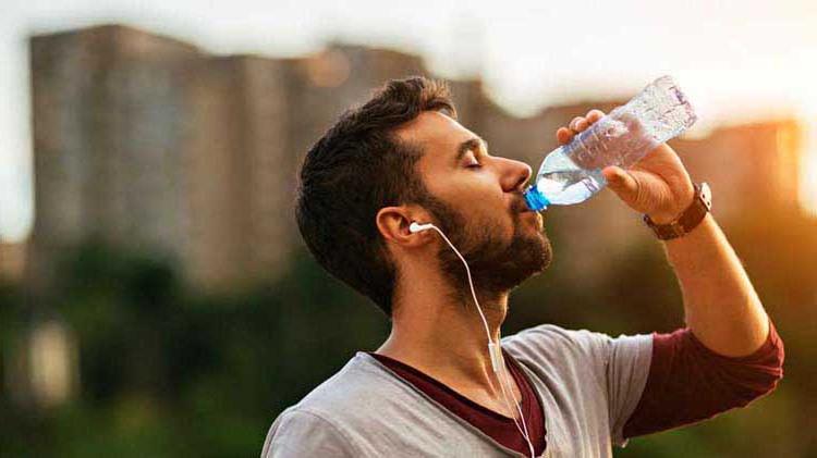 Athletic man drinking water on a humid day to help avoid heat illnesses.