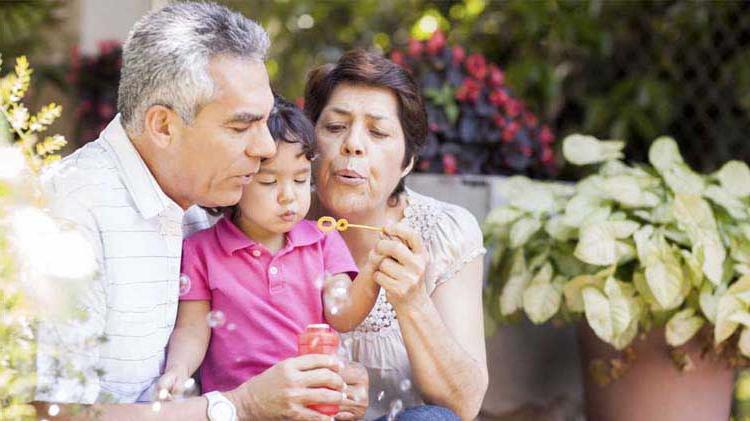 Grandparents with their young granddaughter sitting outside in a garden blowing bubbles.