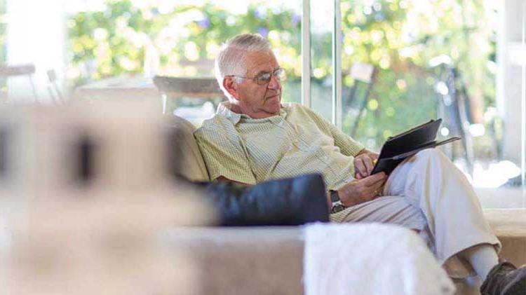 一位年长的绅士坐在扶手椅上阅读有关退休储蓄的书籍.
