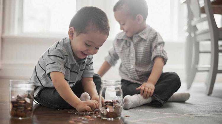 Two little boys are sitting on the floor protecting their finances by placing the coins in jars.