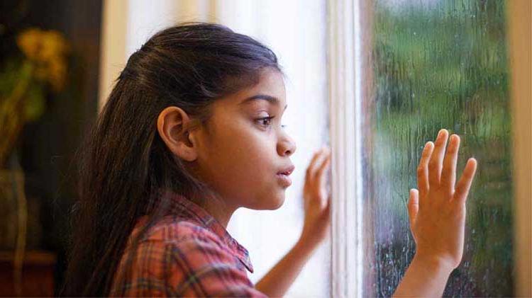 Young girl looking out a storm window.