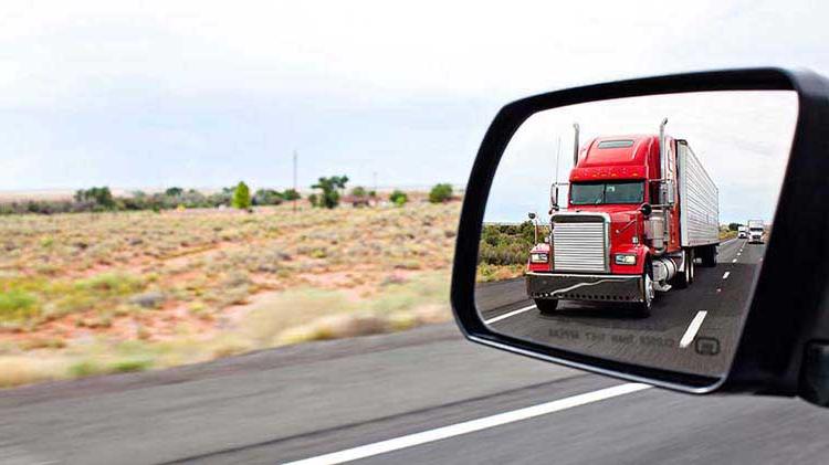Red semi truck shown in the side mirror of a vehicle.
