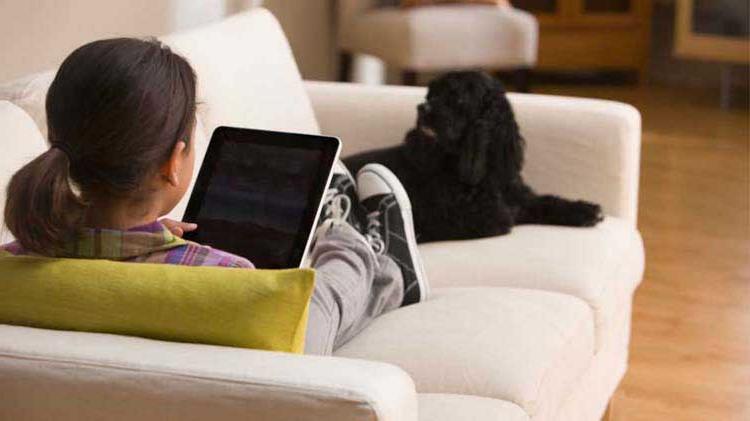 Child alone on couch looking at a tablet.