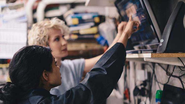 Two woman pointing at a monitor to better understand questions for the mechanic.