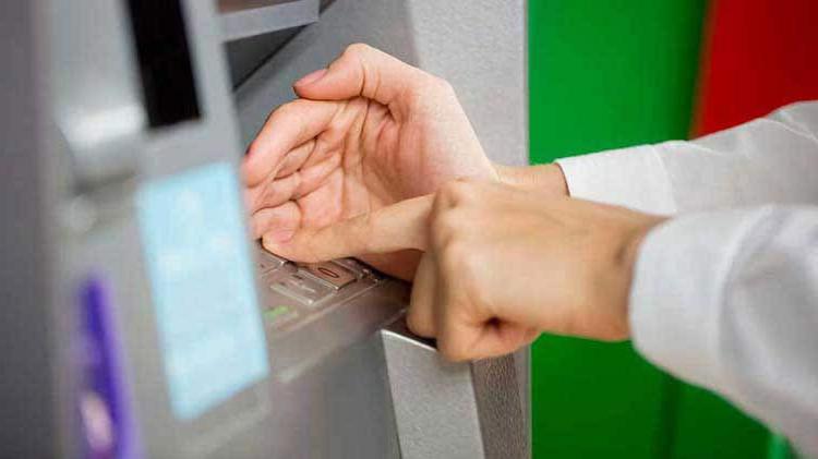 Person's hand entering a PIN number at an ATM machine.