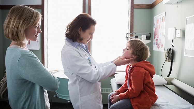 Doctor examining young child with mother watching