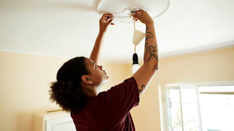 Woman repairing ceiling light fixture with the power shut off.