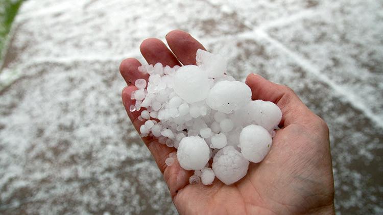 Various sizes of hail being held in a hand after a storm.