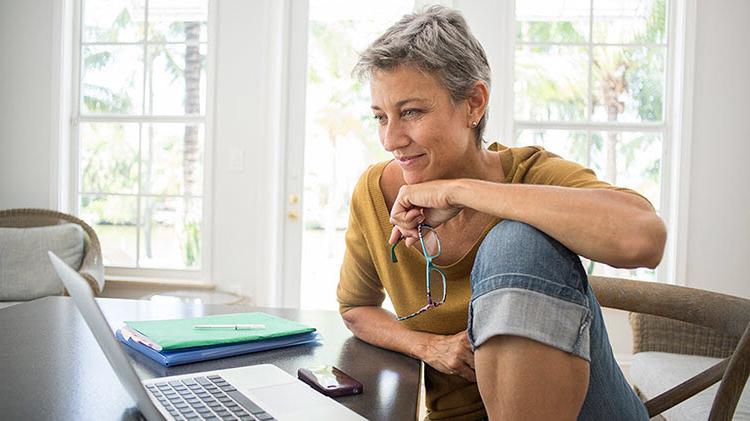 Woman looking at a laptop and thinking about a retirement plan.