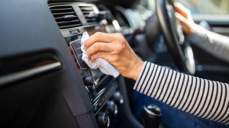 A woman wipes the vent on the dash of her car with a rag