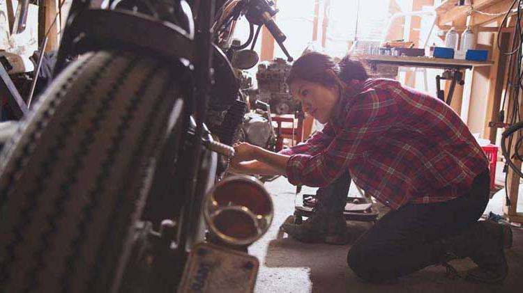 Woman kneeling down working on her motorcycle in a garage.