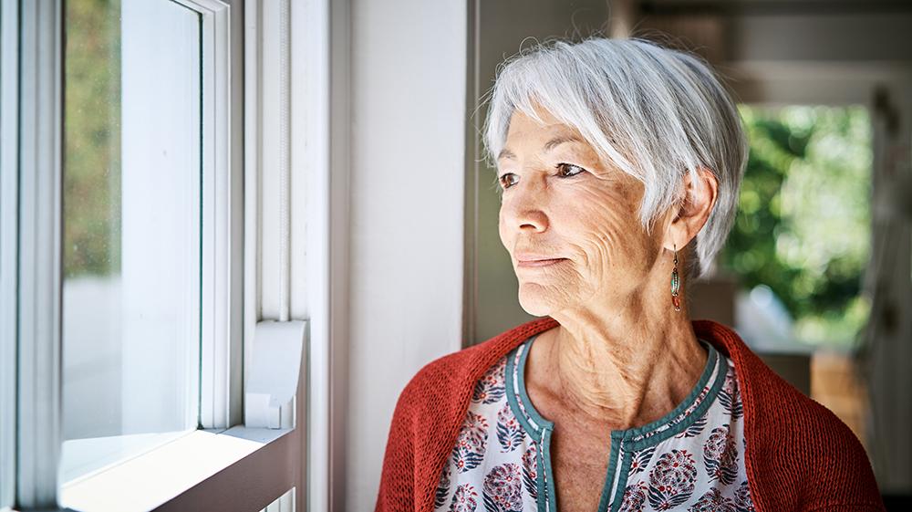 Older woman in a red cardigan gazing out a window.