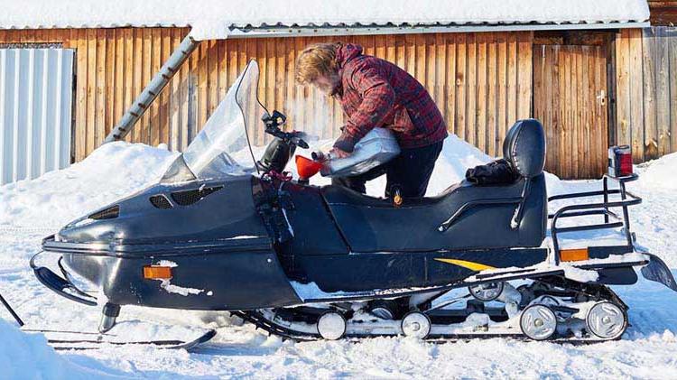 Person outside during winter, adding fuel to their snowmobile.