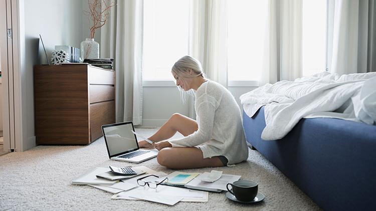Young woman sitting in the floor reviewing paper bills and in a laptop