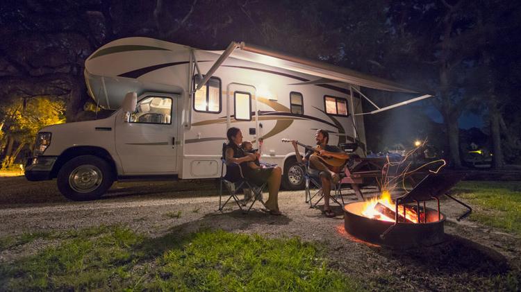 Family sitting around a campfire outside their RV.