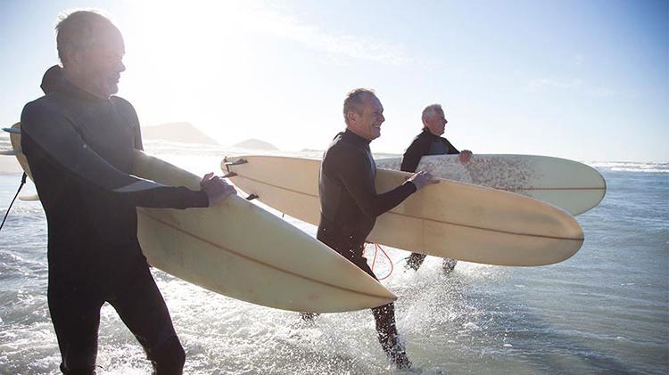 Three retired men are entering the ocean to surf.
